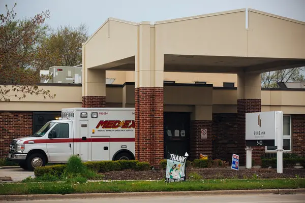 An ambulance is parked outside a brick building with a "Thank You" sign and a "For Sale" sign on the lawn.
