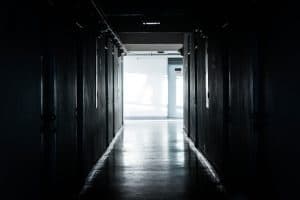A dimly lit hallway leads to a bright, sunlit area at the end.