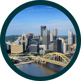Skyline of Pittsburgh with modern skyscrapers and the yellow Fort Pitt Bridge spanning over the river on a clear day.