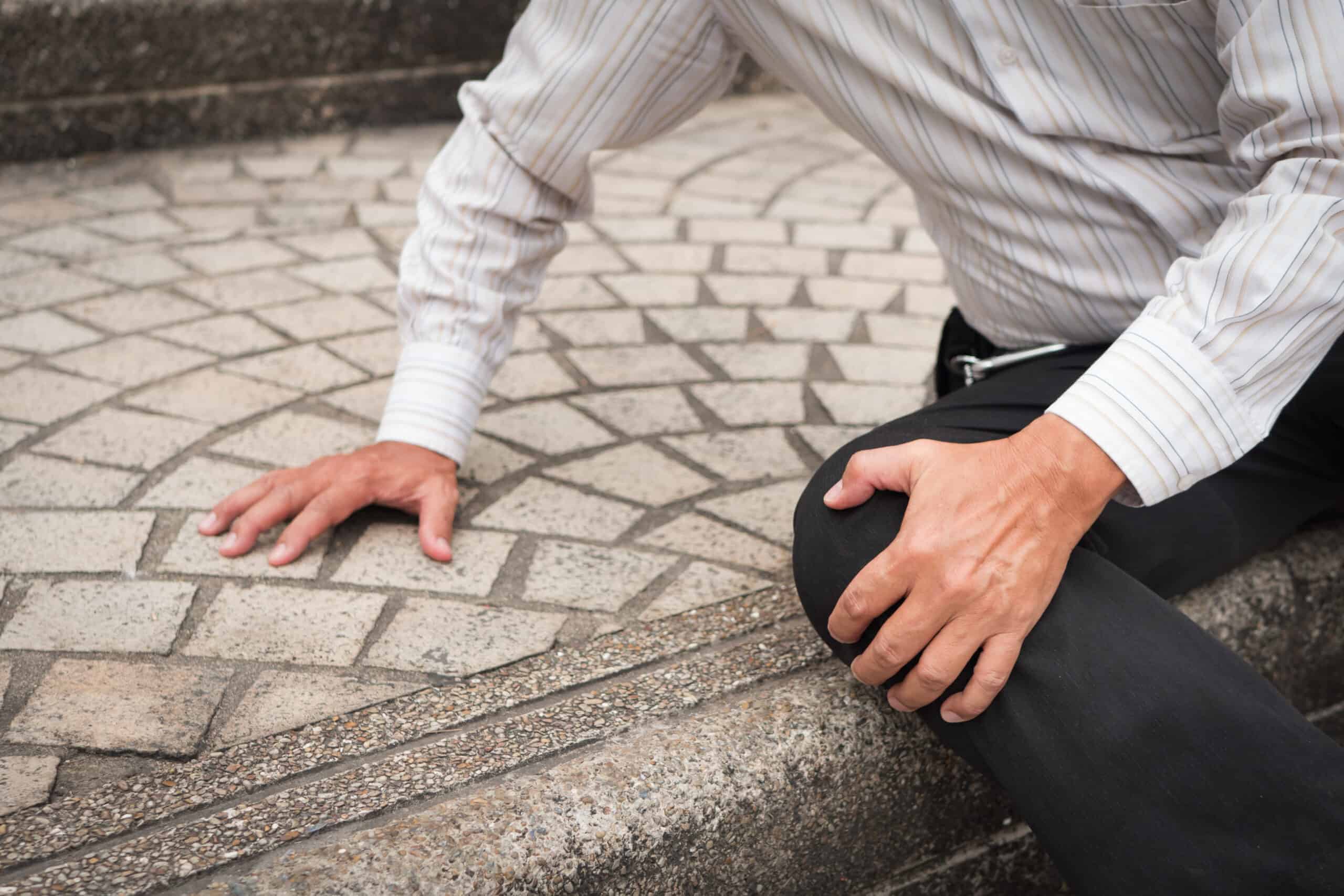 Person in a striped shirt kneeling on tiled steps, holding their knee with one hand and touching the ground with the other.