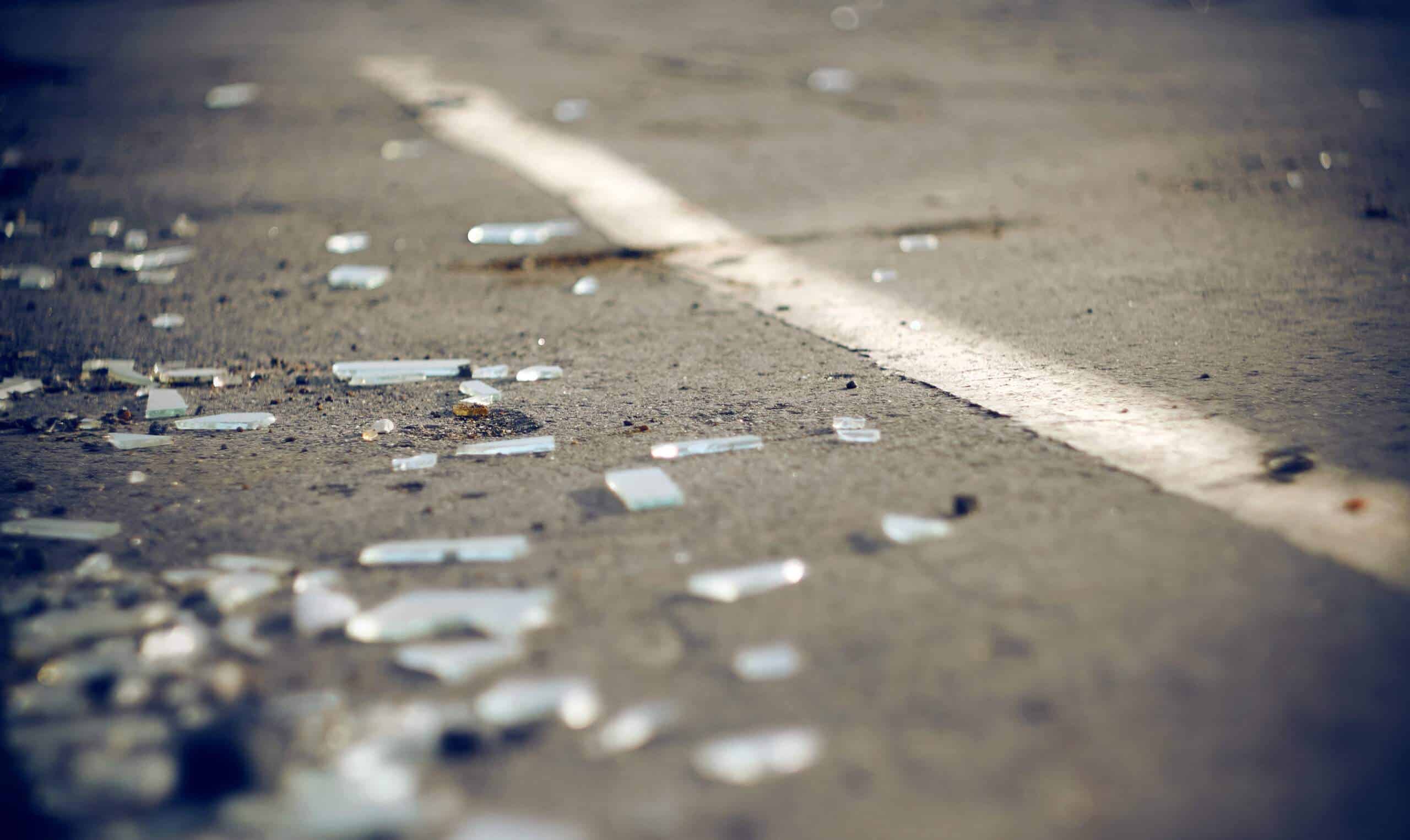 Scattered pieces of broken glass lie on the asphalt near a white traffic line.