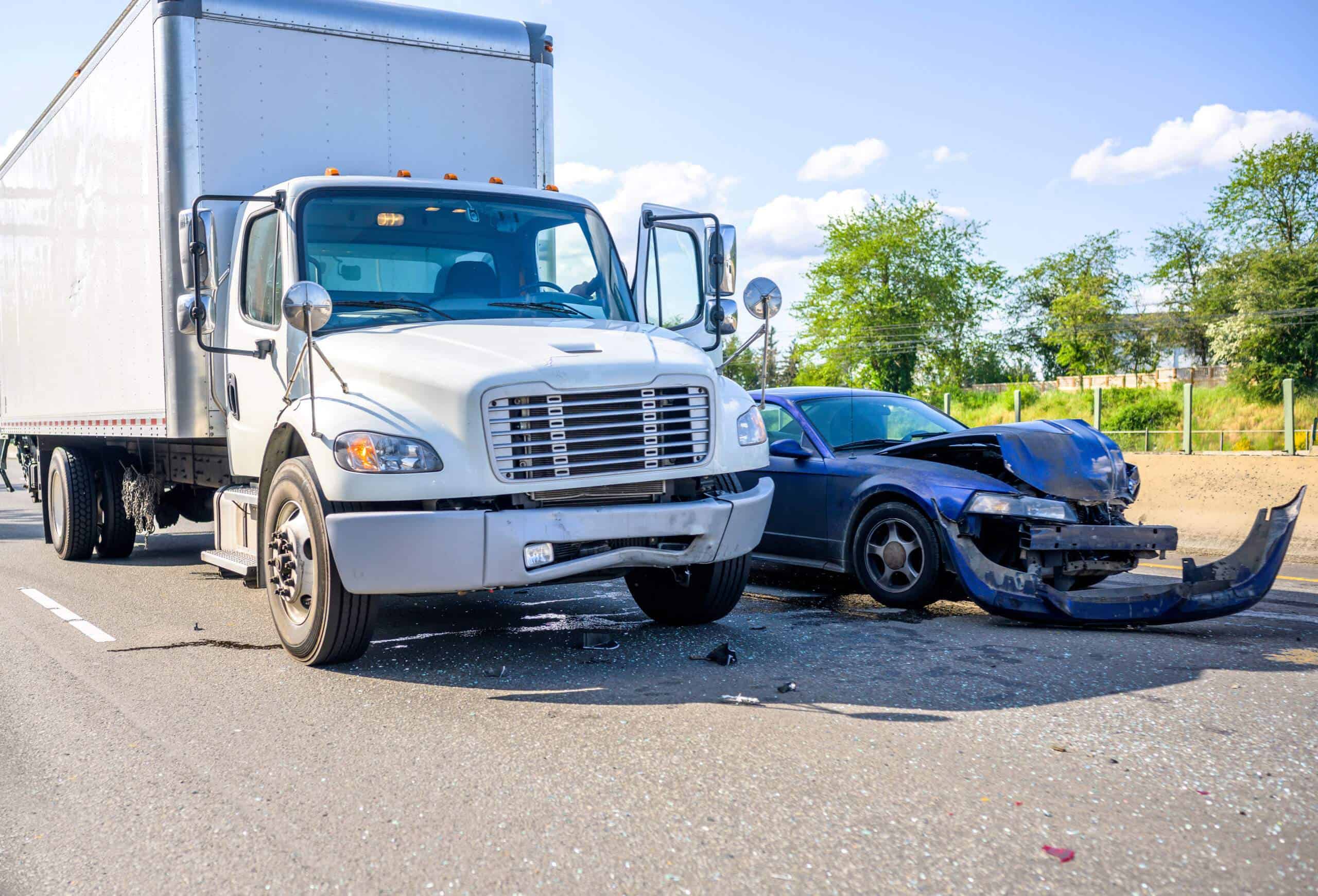 A white truck and a dark car are involved in a collision on a road. Both vehicles show visible damage.