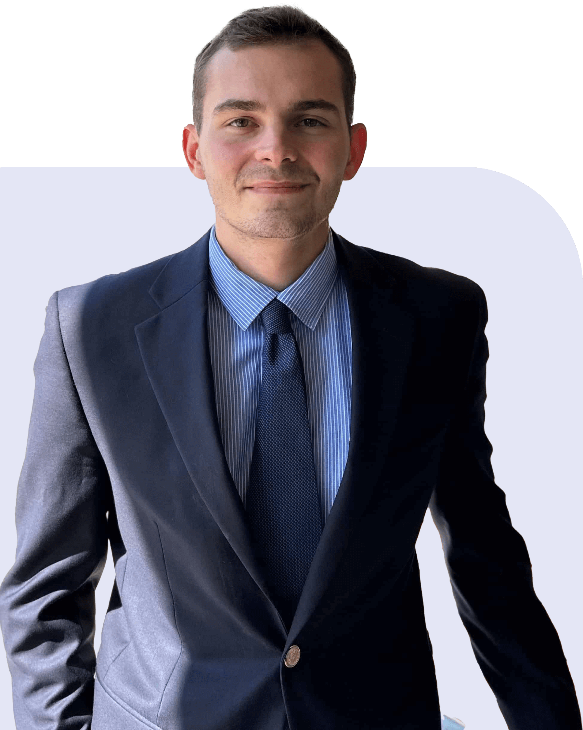 A person in a navy suit and blue tie stands against a light background, looking forward with a slight smile.