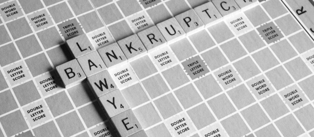 Scrabble board with the words "LAWYER" and "BANKRUPT" intersecting, using black and white tiles.