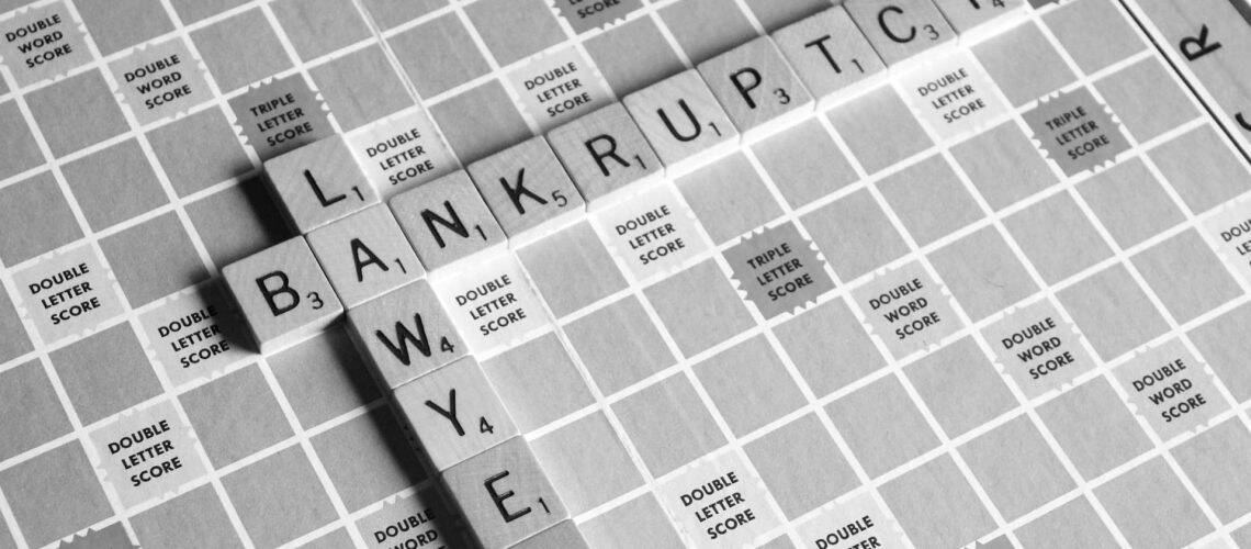 Scrabble board with the words "LAWYER" and "BANKRUPT" intersecting, using black and white tiles.