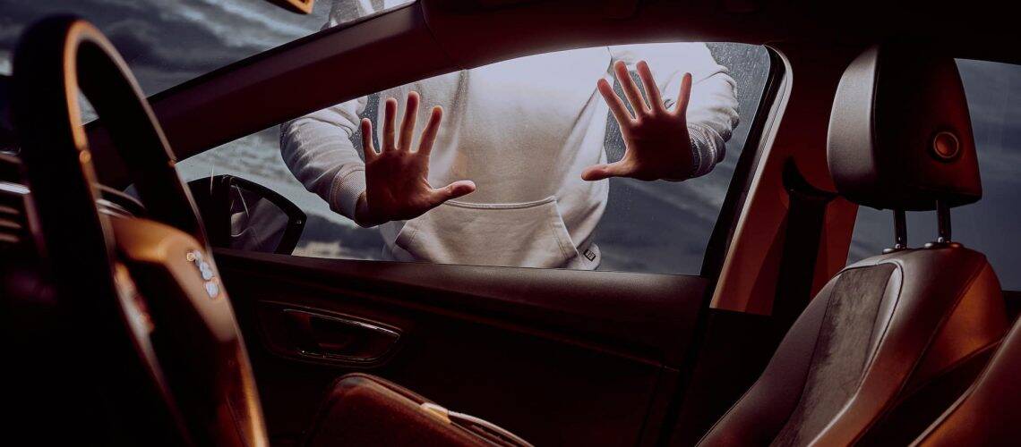 Person in a hoodie pressing hands against the car window, viewed from inside an empty vehicle with a partially visible seat.