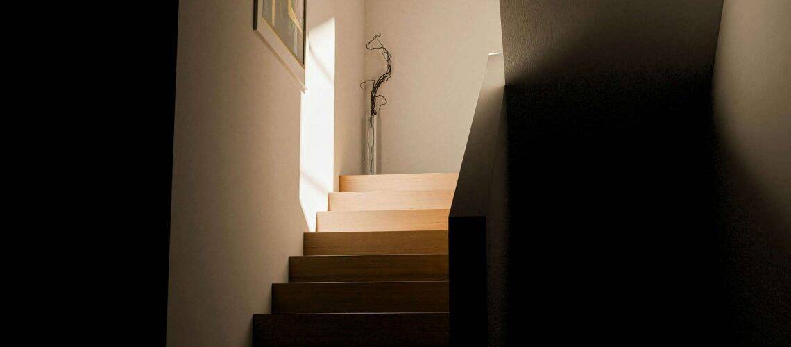 Wooden staircase leading to a bright hallway with a tall vase and dried branches.