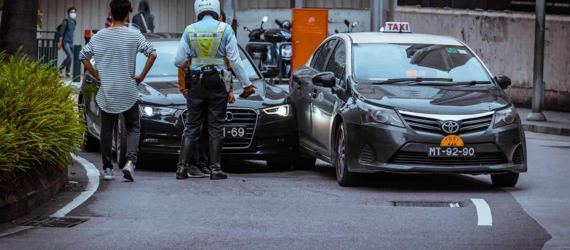 A police officer and a man stand near two cars involved in a minor collision on a city street.
