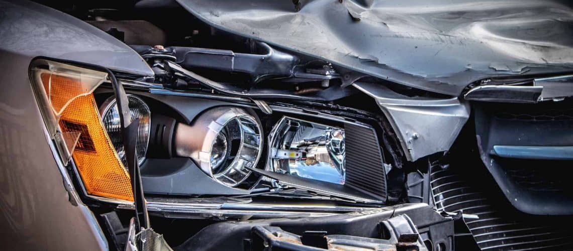 Close-up of a damaged car front, showing a broken headlight and crumpled metal.