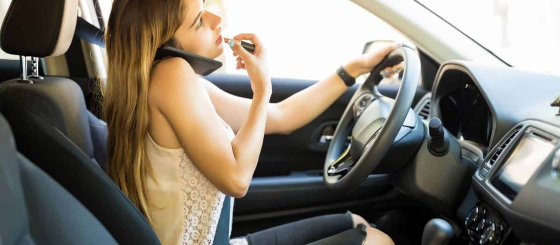 A woman applies lipstick while talking on the phone and driving a car.