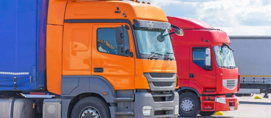 Two parked trucks: an orange truck on the left and a red truck on the right, set against a blue sky.