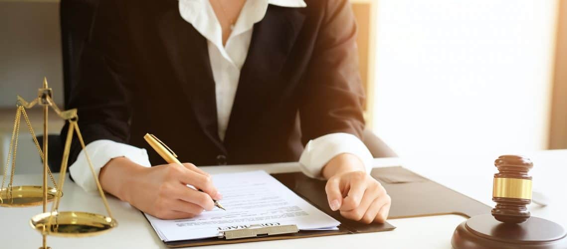 Person in a suit signing a contract at a desk, with a gavel and justice scales nearby.