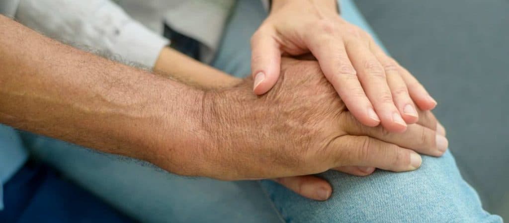 Two hands resting on a knee, one appearing older and the other younger, on a blue fabric background.