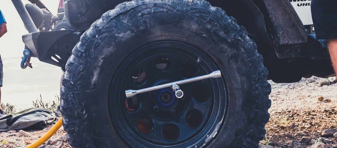 Close-up of an off-road vehicle tire with a lug wrench attached, on a rocky terrain.