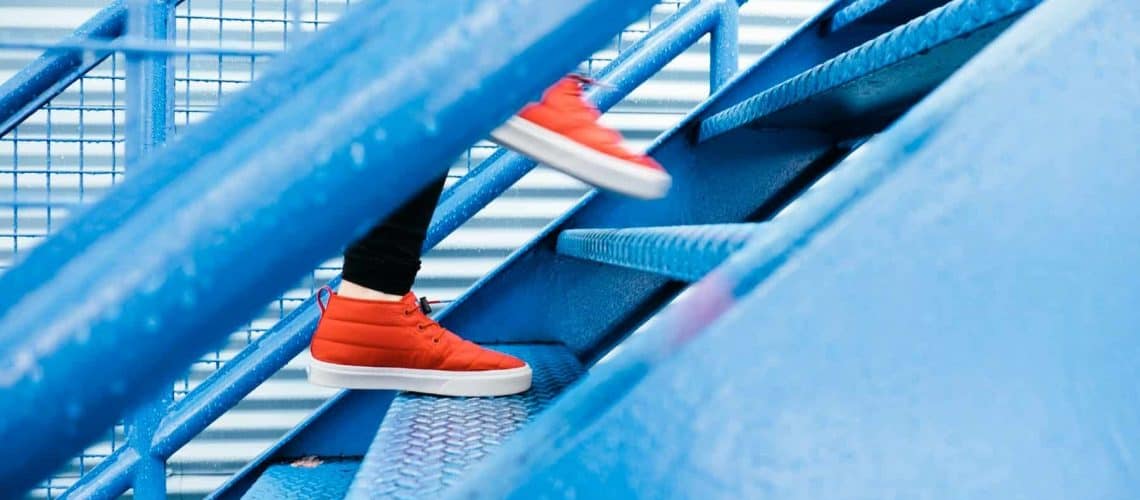 Person wearing red sneakers walking up blue metal stairs.