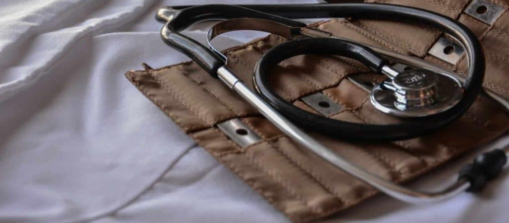 A stethoscope lies on a folded, light-colored cloth next to a brown, fabric medical pouch.