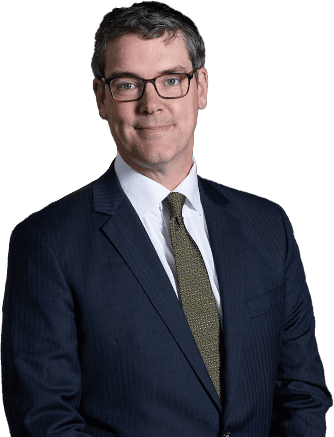 Man in a dark suit and glasses standing against a plain background.