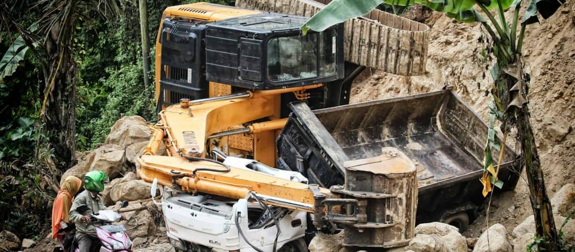 Excavator and dump truck involved in a landslide accident; a motorcycle with two riders nearby.