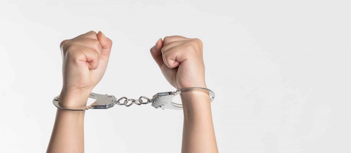 Two hands in metal handcuffs are raised against a plain white background.