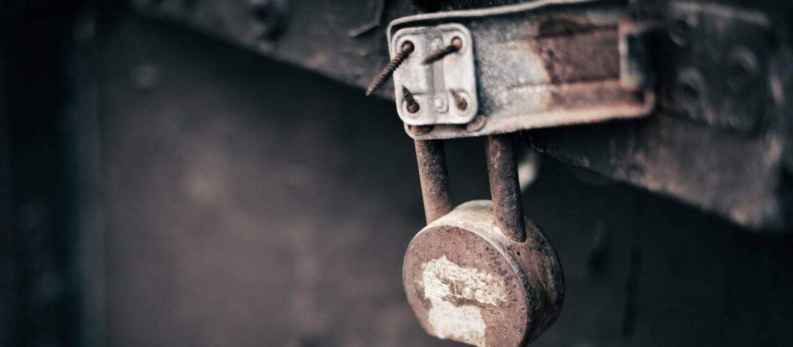 A rusty padlock hangs on a metal latch affixed to a weathered wooden surface.