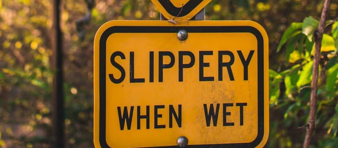 A yellow road sign reading "Slippery When Wet" is surrounded by green foliage.