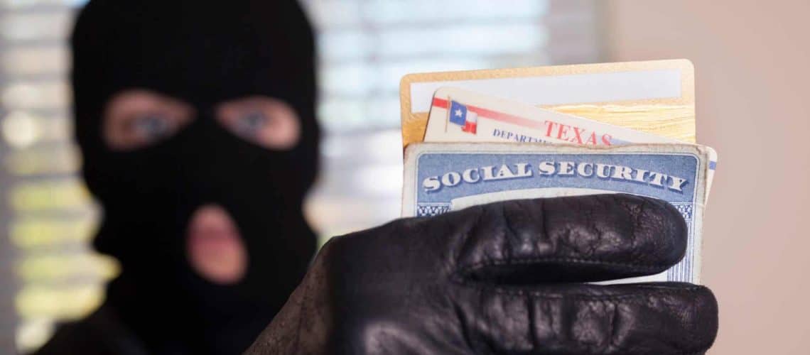Person in a black balaclava and gloves holding a Social Security card and various IDs.