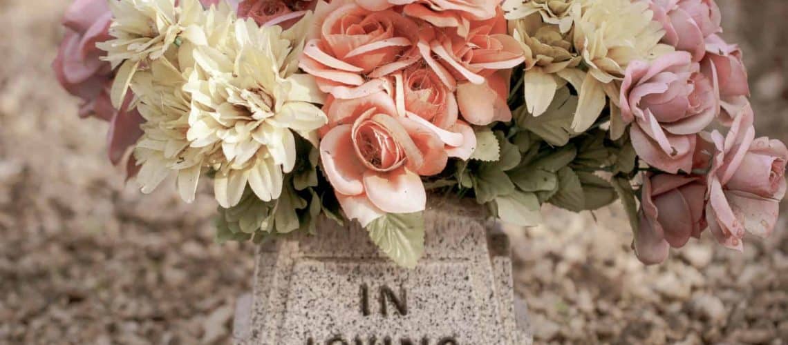 A bouquet of pink and yellow roses on a stone grave marker inscribed with "IN LOVING.