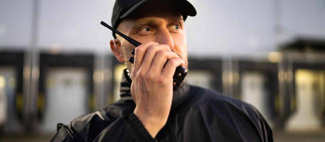 A person in a cap and jacket uses a handheld radio for communication.