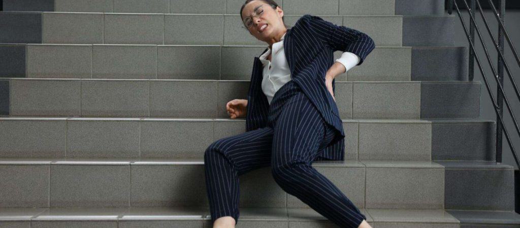 Person in a suit sitting on stairs holding their lower back, appearing to experience discomfort.