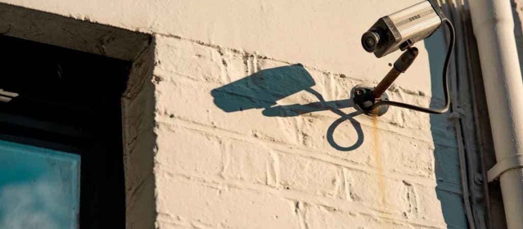 A security camera mounted on a white brick wall casts a shadow.