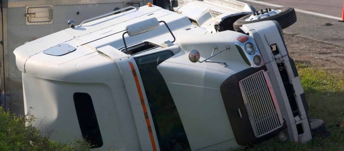 White semi-truck overturned on its side on a grassy area by the roadside.