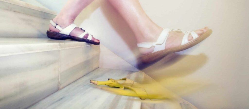 Person in white sandals slipping on a banana peel while descending marble stairs.