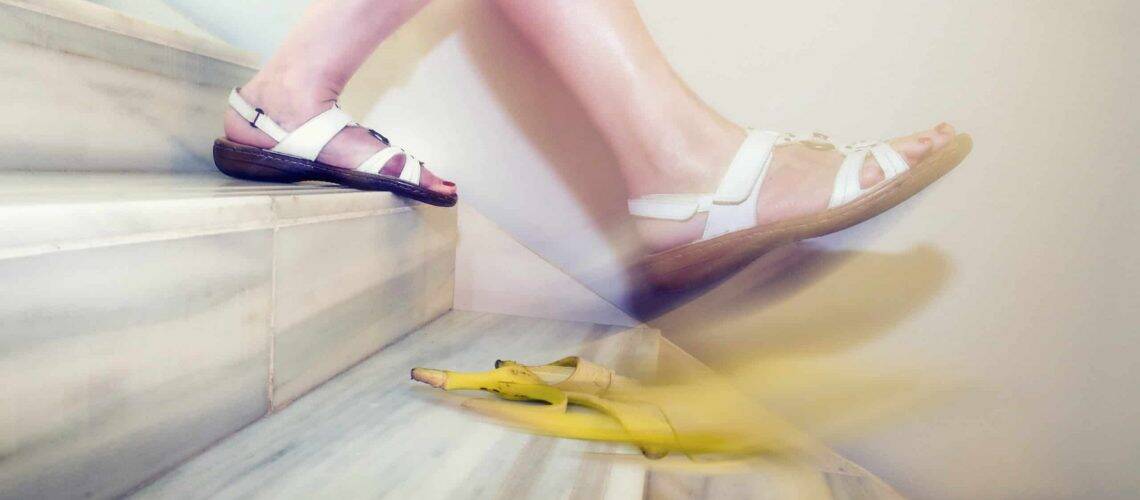 Person in white sandals slipping on a banana peel while descending marble stairs.